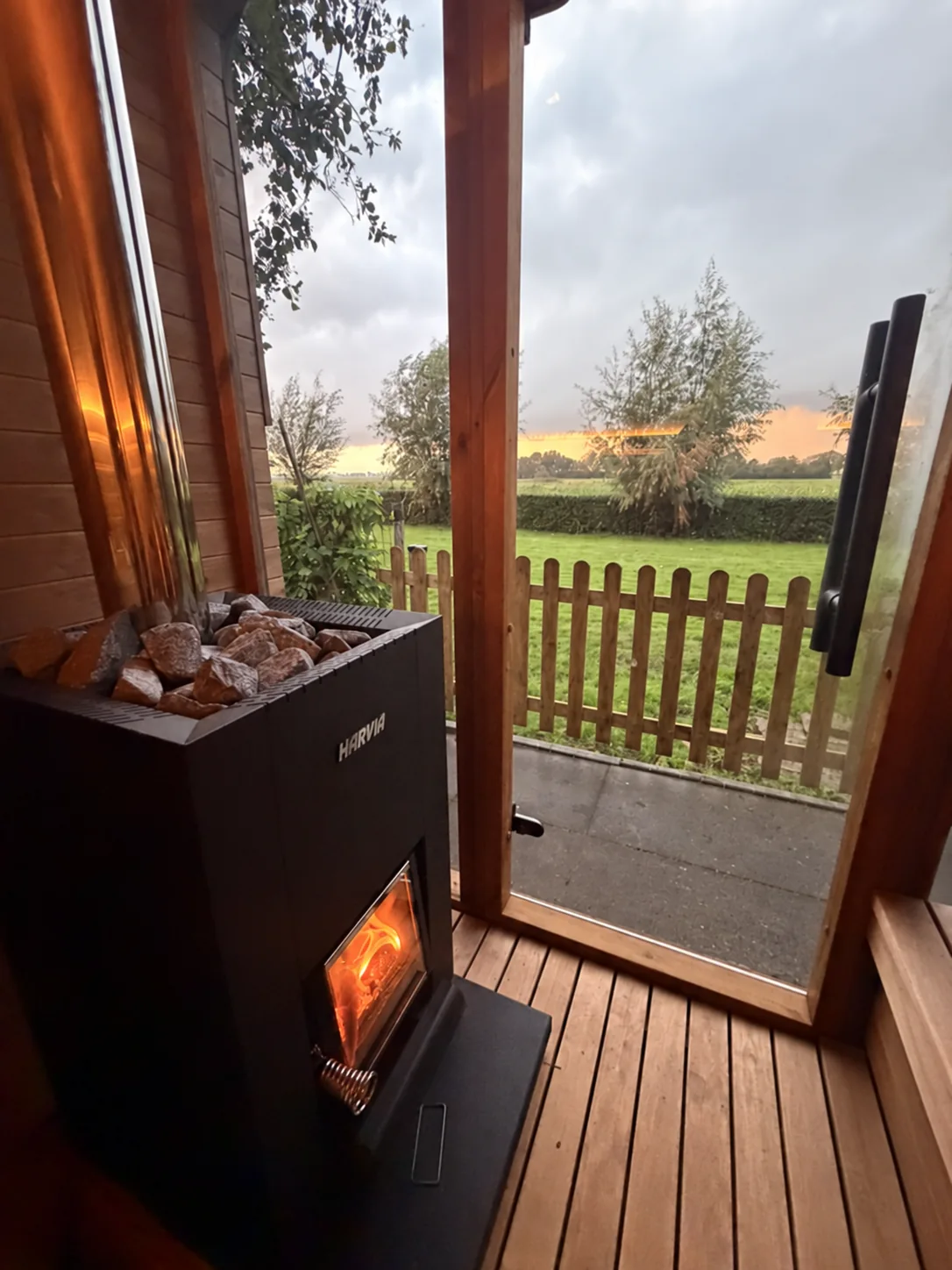 Uitzicht vanuit de houtgestookte sauna op de tuin en het landschap, met het vuur in de kachel